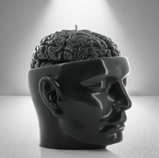 A dark grey soy candle shaped like a human head with an exposed brain design, featuring a wick on top. Sleek and detailed.