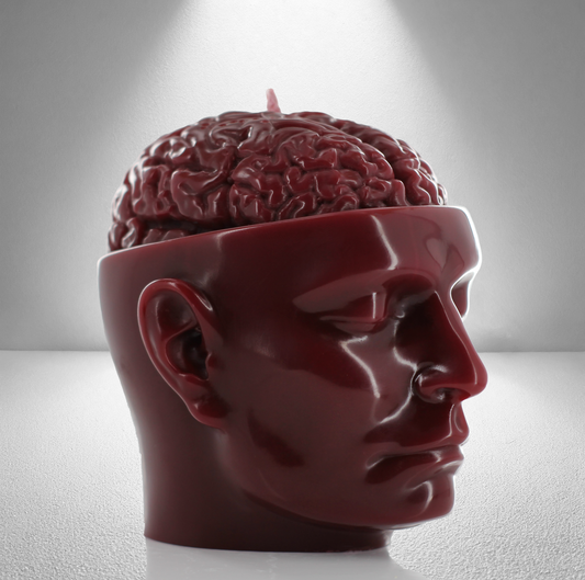 A dark red soy candle shaped like a human head with an exposed brain design, featuring a wick on top. Bold and detailed.