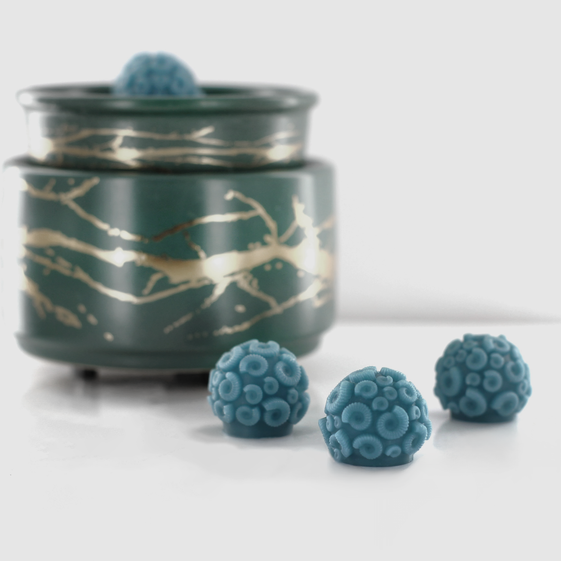 Aqua Blue fragranced wax melts shaped like ammonites with intricate spiral details, displayed alongside a decorative wax warmer with a gold branch design.