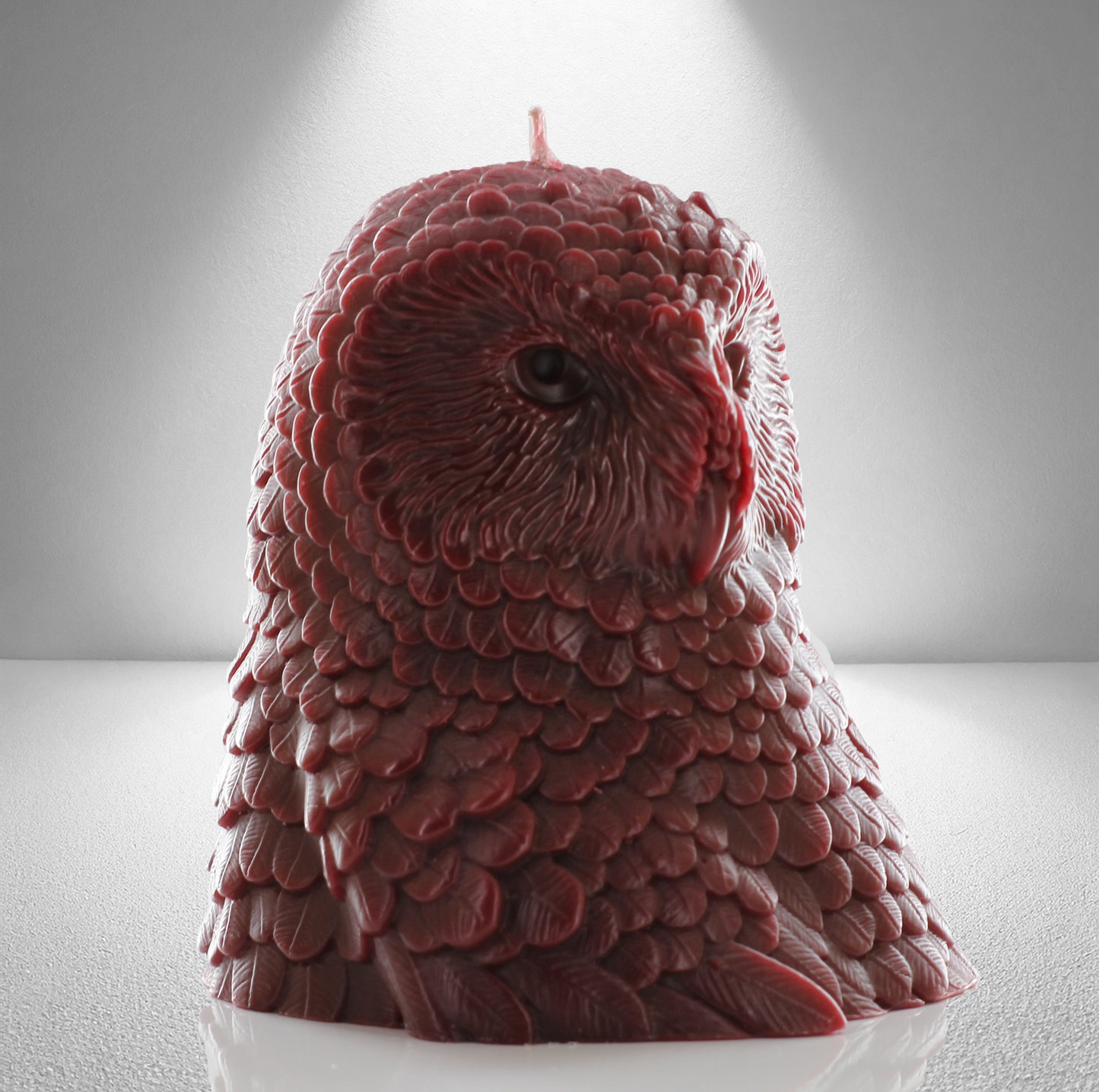 Dark red owl shaped candle with detailed feather design, set against a gray background