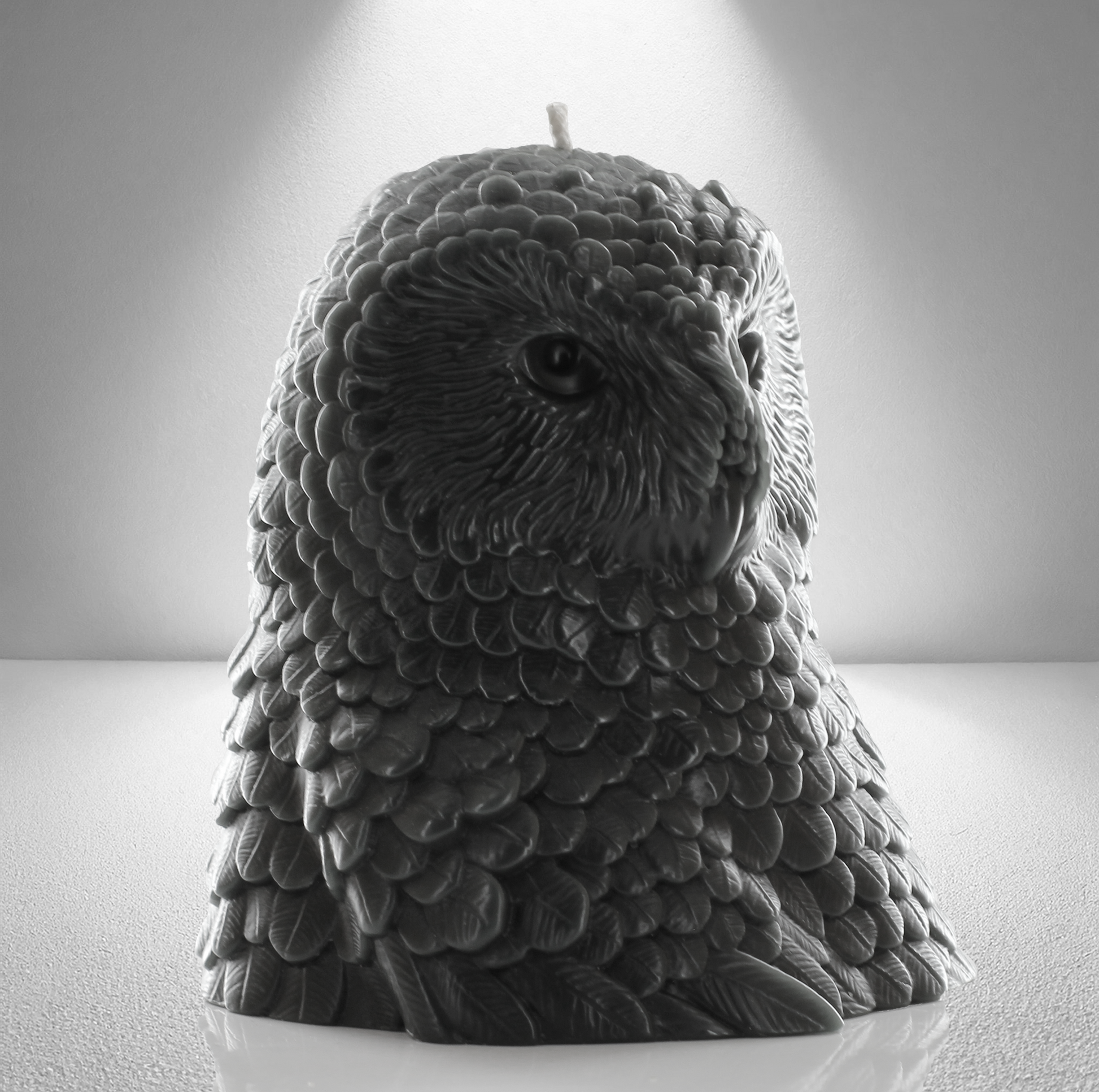 Dark grey owl shaped candle with detailed feather design, set against a gray background