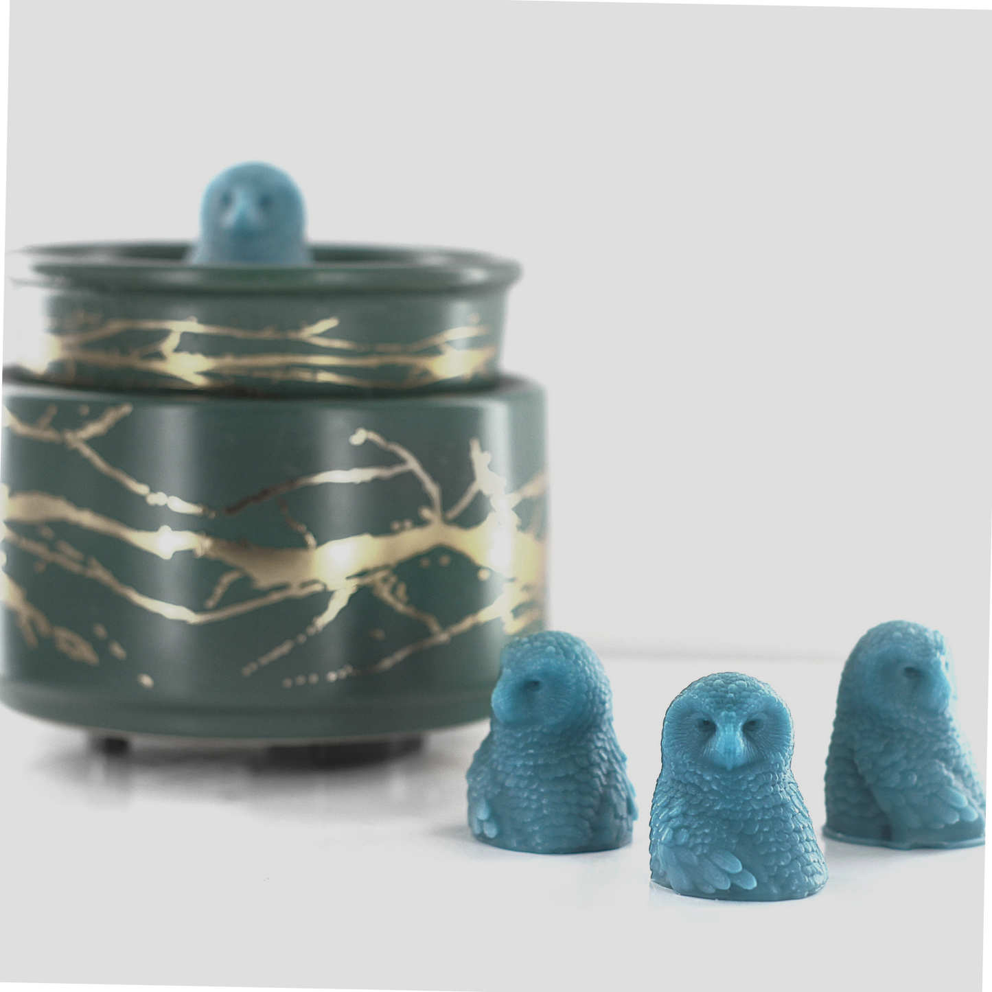 Fragranced wax melts shaped like detailed blue owls, displayed alongside a decorative wax warmer with a gold branch design.