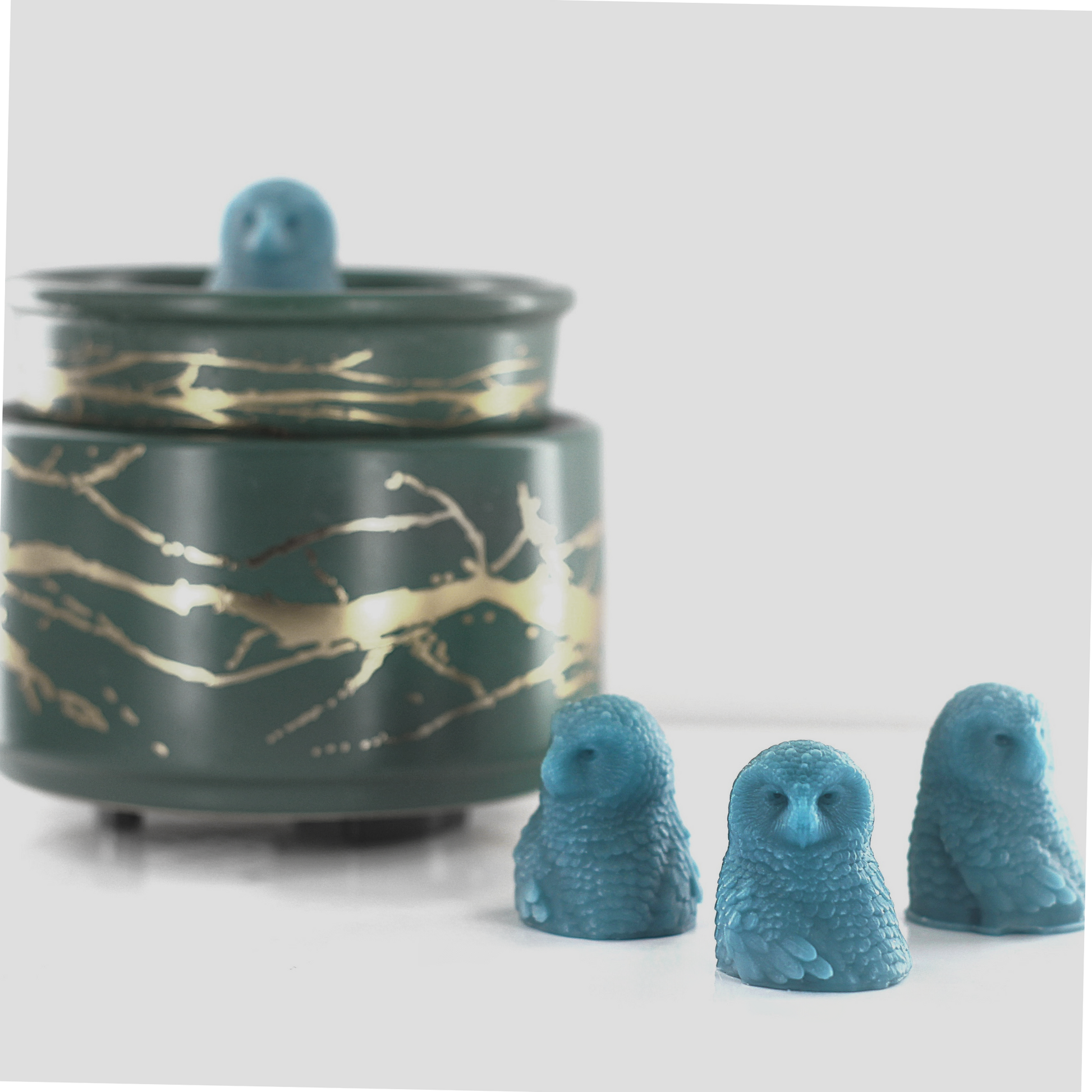 Fragranced wax melts shaped like detailed blue owls, displayed alongside a decorative wax warmer with a gold branch design.