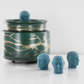 Aqua blue fragranced wax melts shaped like miniature human heads with exposed brains, displayed near a decorative wax warmer with a gold branch design.