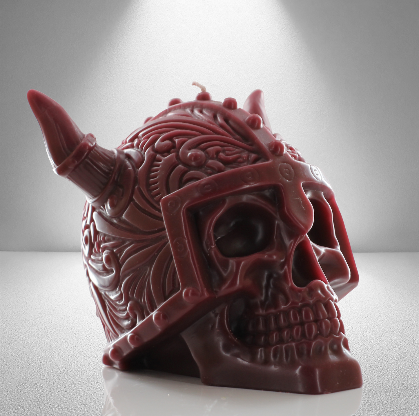 Part side view of a dark red unscented candle shaped like a Viking skull with intricate details and a horned helmet design. Bold and striking.