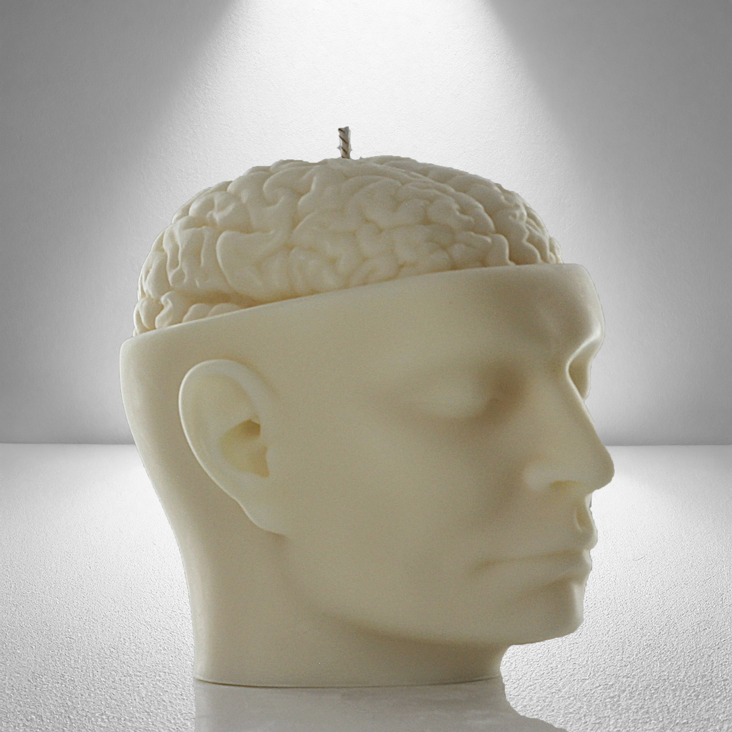 Soy candle shaped like a human head with an exposed brain design, featuring a wick on top. Cream-colored with fine details