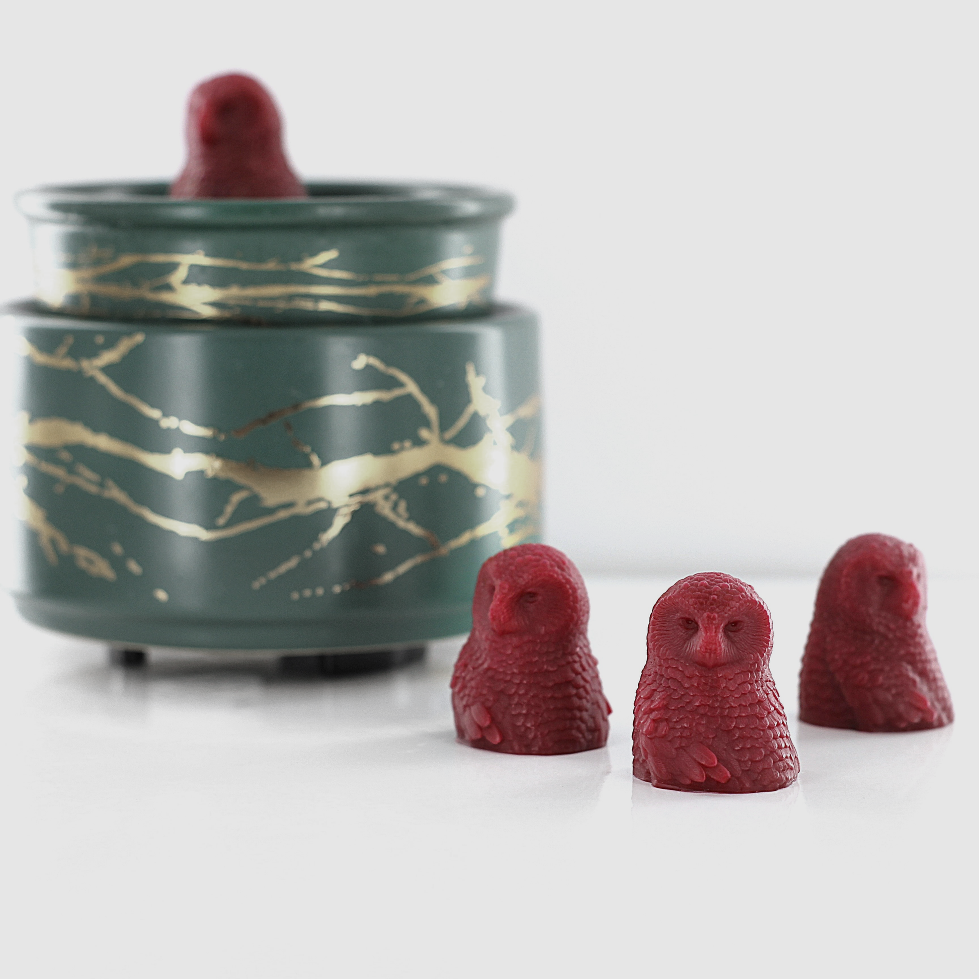 Fragranced wax melts shaped like detailed red owls, displayed alongside a decorative wax warmer with a gold branch design.