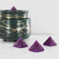 Purple fragranced wax melts shaped like pyramids with intricate details, displayed next to a decorative wax warmer with a gold branch design.